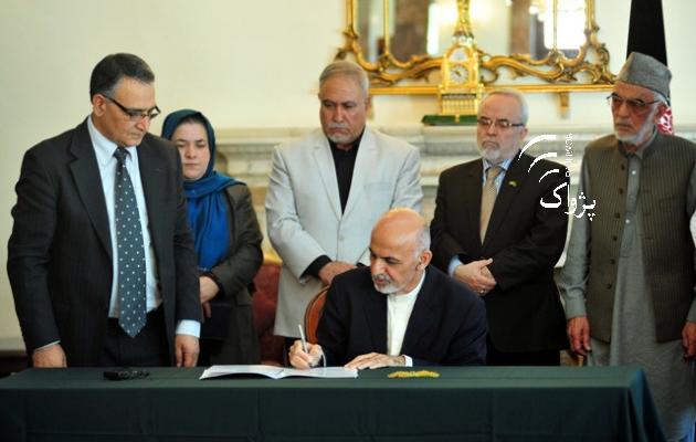 President signs a document flanked by a number of officials.